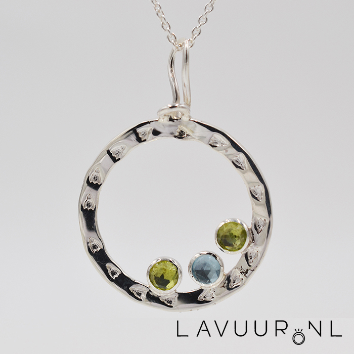 Zilveren hanger in cirkelvorm, waarbij de cirkel gedecoreerd is met fantasiestempels, onderin de cirkel drie ronde zettingen met topaas en peridoots