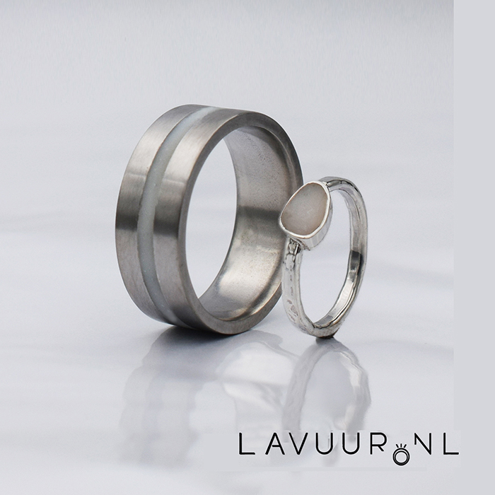 twee trouwringen, een brede ring gemaakt van zirkonium met in het midden een band gevuld met moedermelk en hars en een kleine zilveren ring met een fantasievorm zetting waarin moedermelk met hars zit
