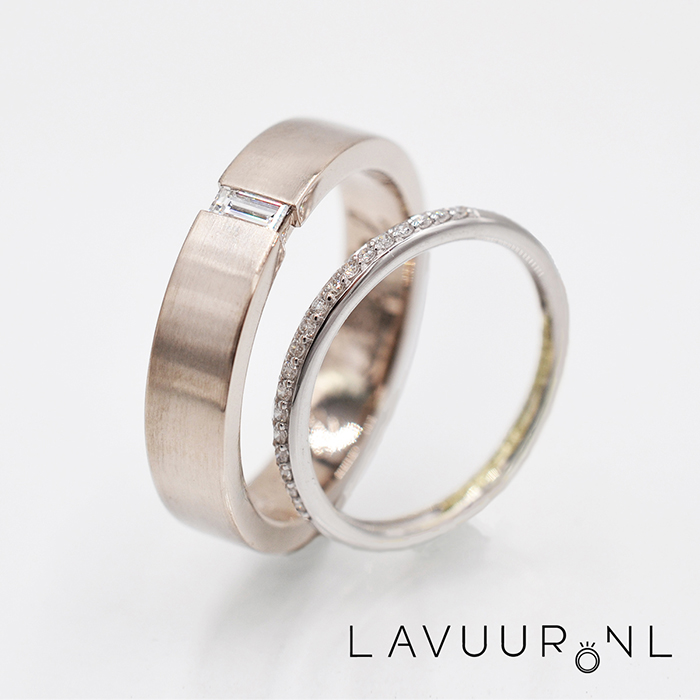 twee witgouden trouwringen, waarbij de linker ring breed is met een rechthoekige diamant die tussen de band geklemd zit en de rechter ring smal is en rondom gezet met kleine diamantjes