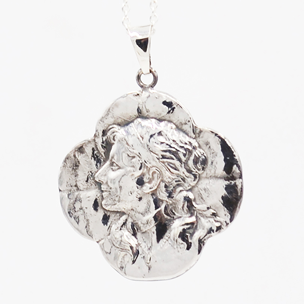 zilveren hanger waarin een vrouwenhoofd kijkend naar links op een ondergrond van een klavertje vier in de Art Nouveau stijl gestempeld is