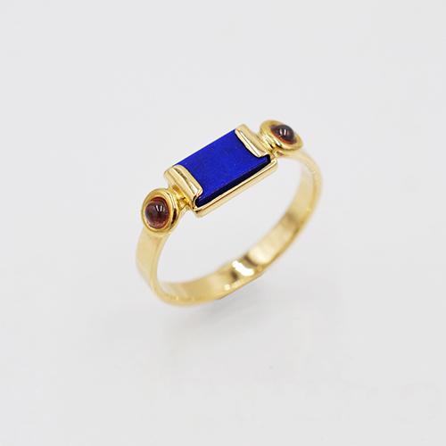 gouden zegelring met rechthoekige vlakke lapis lazuli in het midden en aan beide kanten een kleine ronde granaat in ronde draadzetting