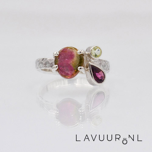 zilveren ring met gehamerde scheen met in het midden een platte gladde watermeloen toermalijn en rechts ernaast gearrangeerd twee edelstenen een ronde spinel en een peervormige rhodoliet